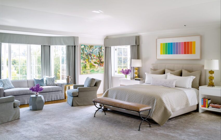 Spacious bedroom with a king-size bed, colorful artwork, large windows, and elegant decor in soft neutral tones.