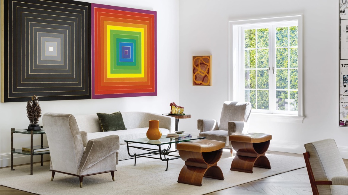 Modern living room with abstract wall art, beige furniture, glass coffee table, and large window with natural light.