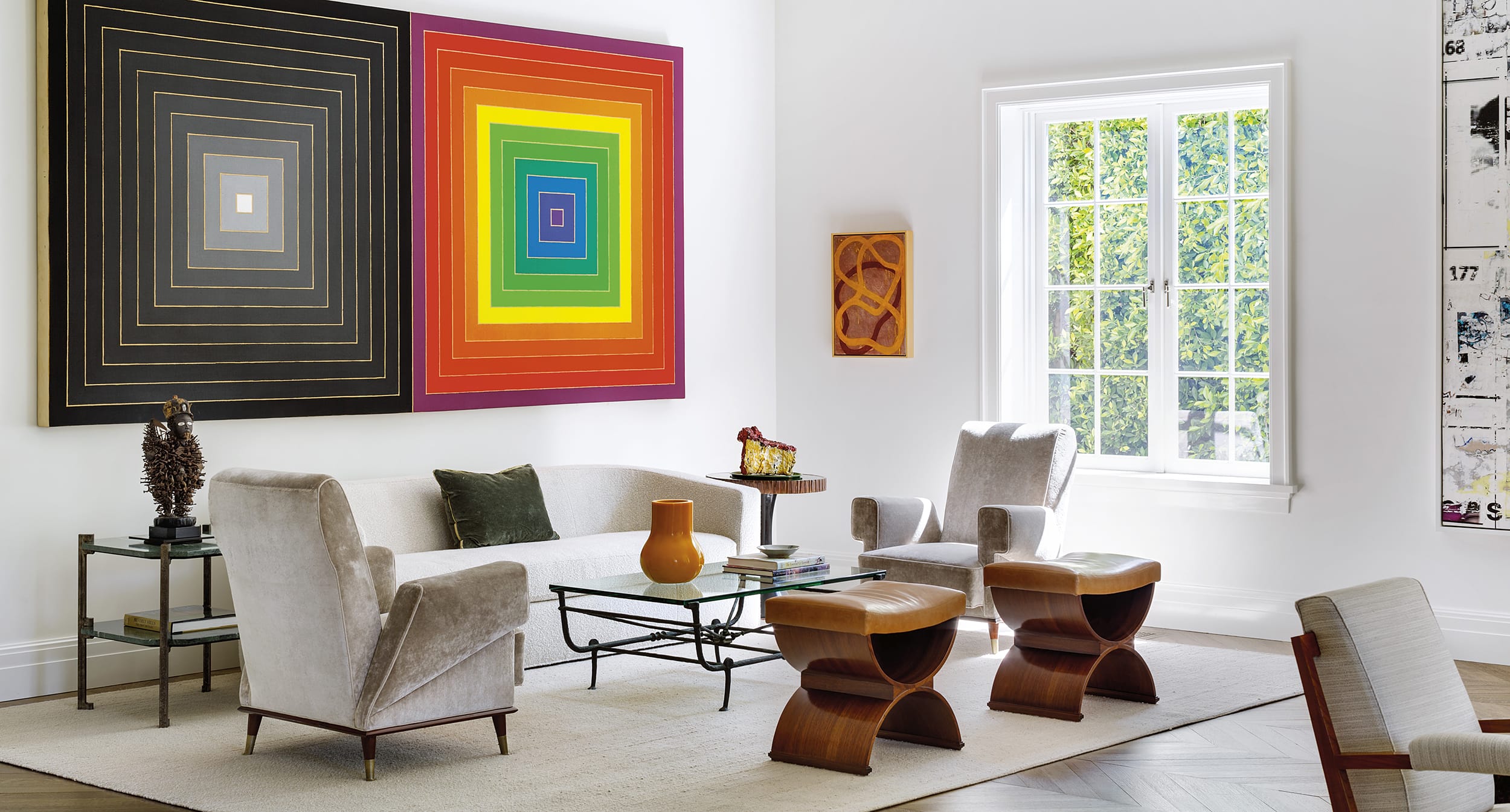 Modern living room with abstract wall art, beige furniture, glass coffee table, and large window with natural light.