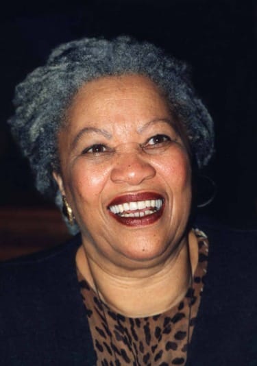 Smiling woman with gray hair, wearing a dark top and earrings, against a dark background.