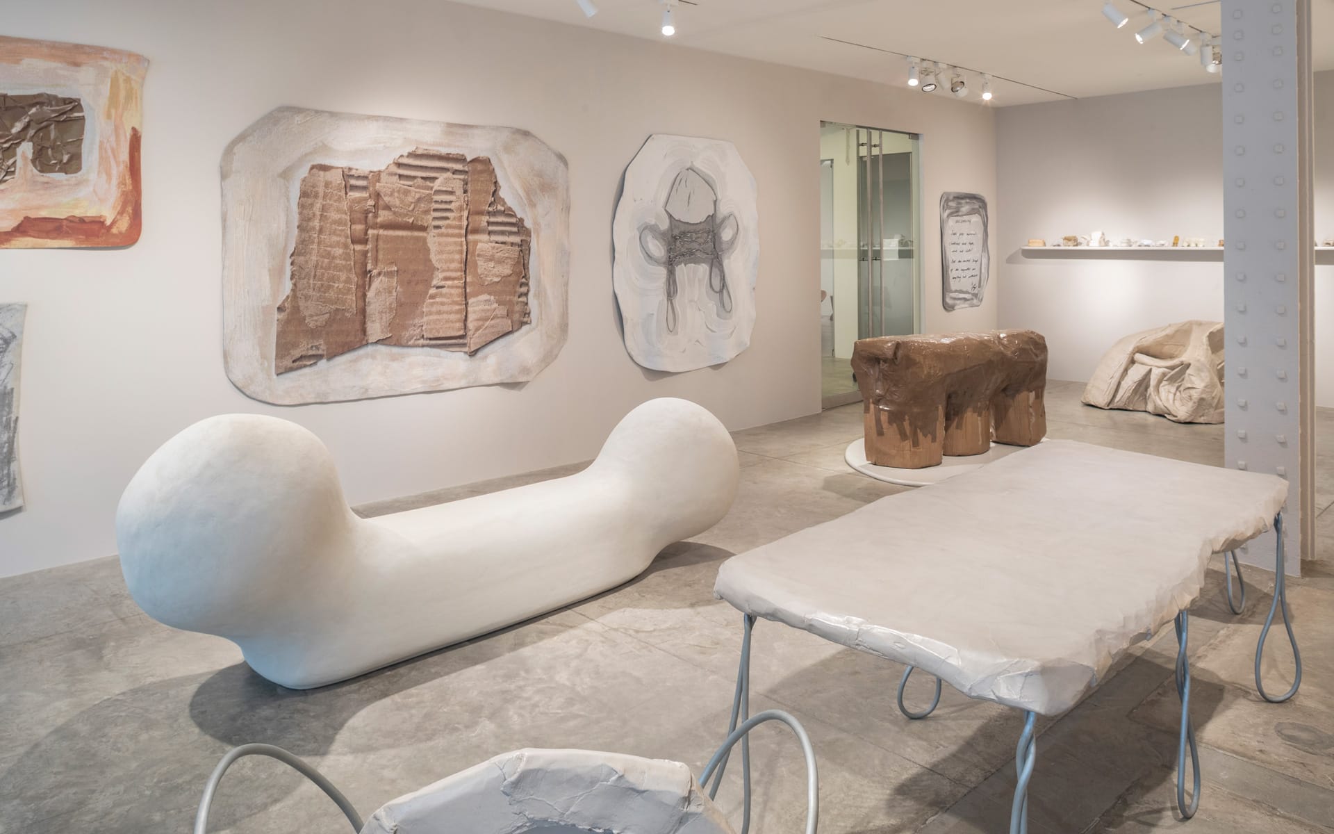 Contemporary art gallery with abstract sculptures and wall-mounted artworks in a minimalist setting.
