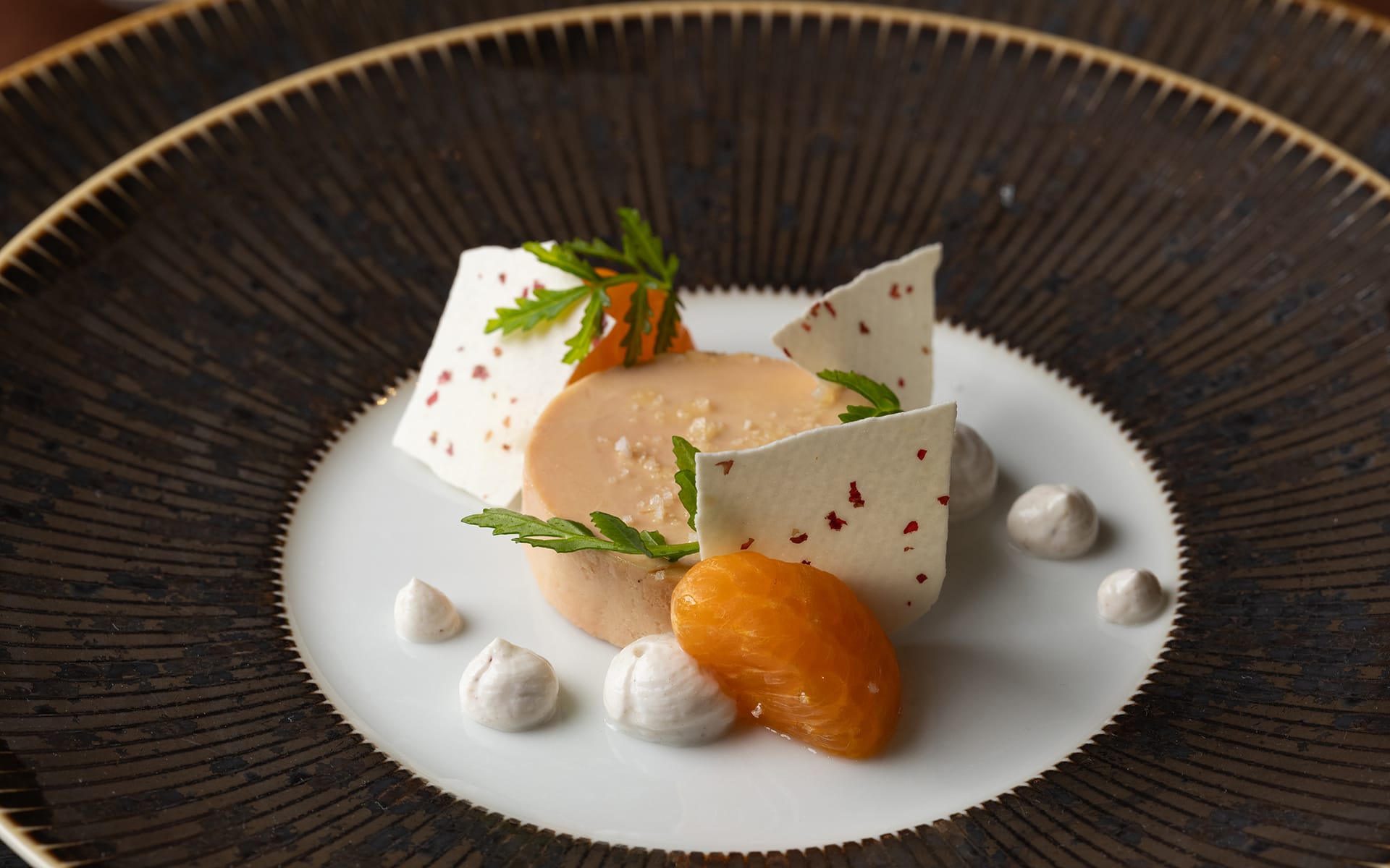 Gourmet dessert with mousse, meringue pieces, whipped cream dots, and a mandarin segment on an elegant plate.