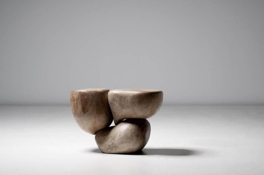 Modern wooden sculpture with three interlocking, rounded shapes resting on a smooth, light-colored floor.