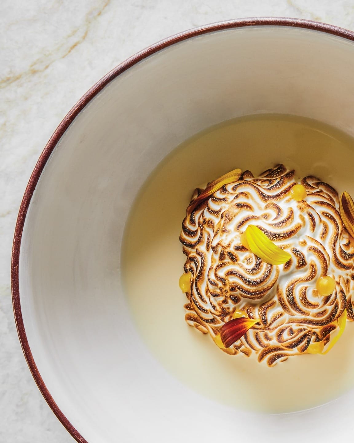 Baked Alaska dessert with toasted meringue swirls on a white plate, garnished with small edible flowers.