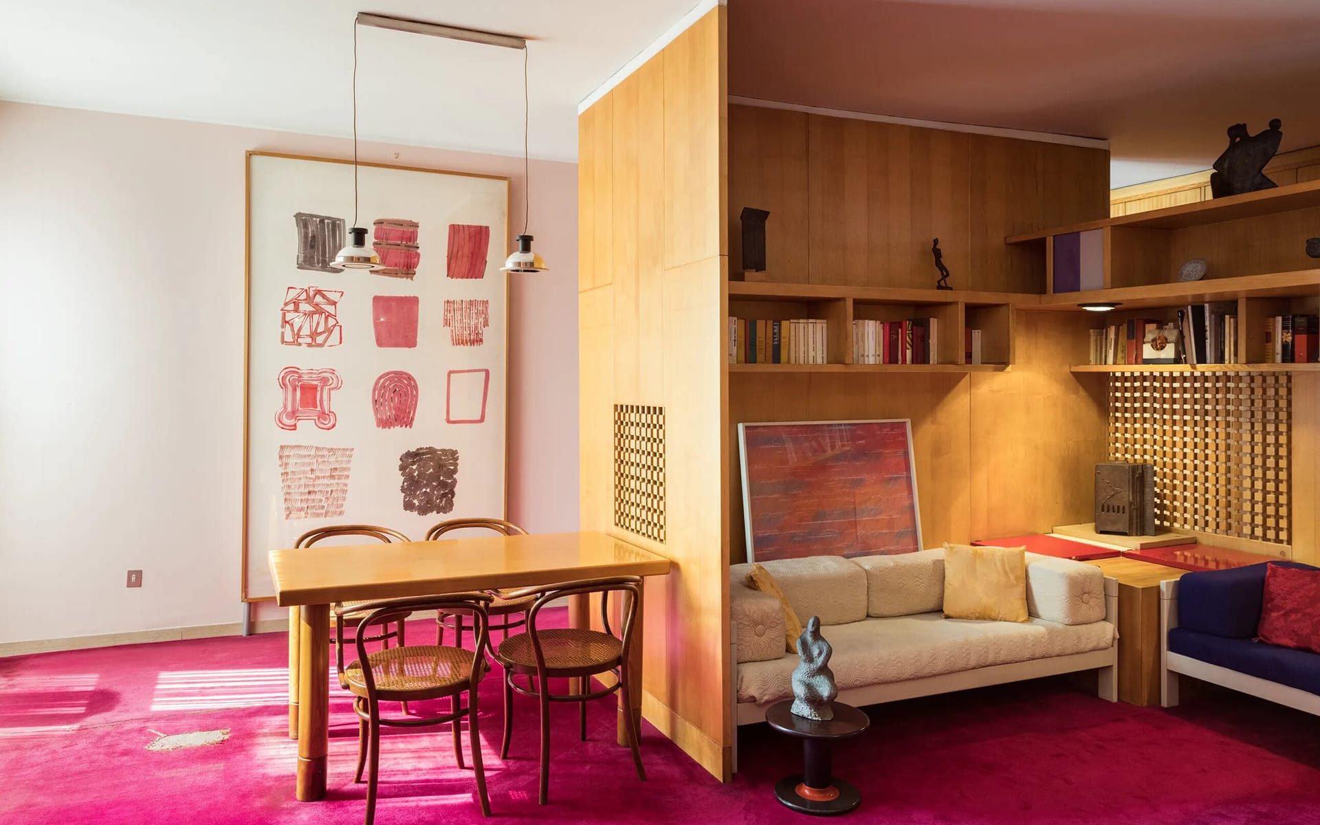 Mid-century modern living room with red carpet, wooden furniture, abstract art, and a cozy seating area with bookshelves.