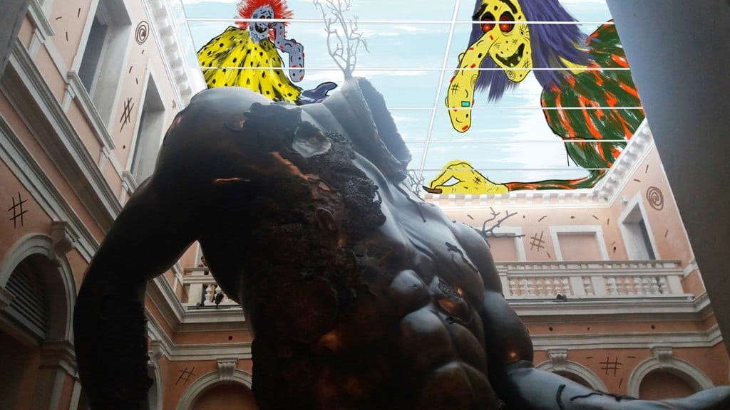 Headless sculpture in a classic courtyard with colorful, abstract monsters painted on the glass ceiling above.