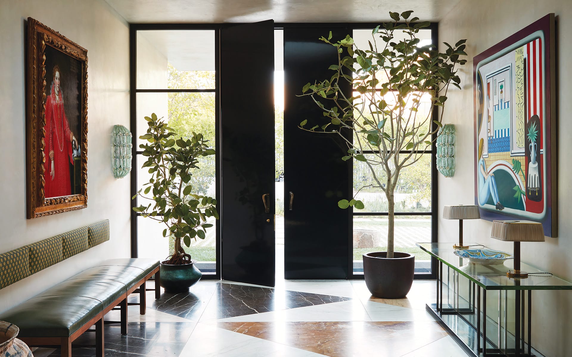 Elegant foyer with large black doors, a bench, indoor plants, and art on the walls, featuring natural light.