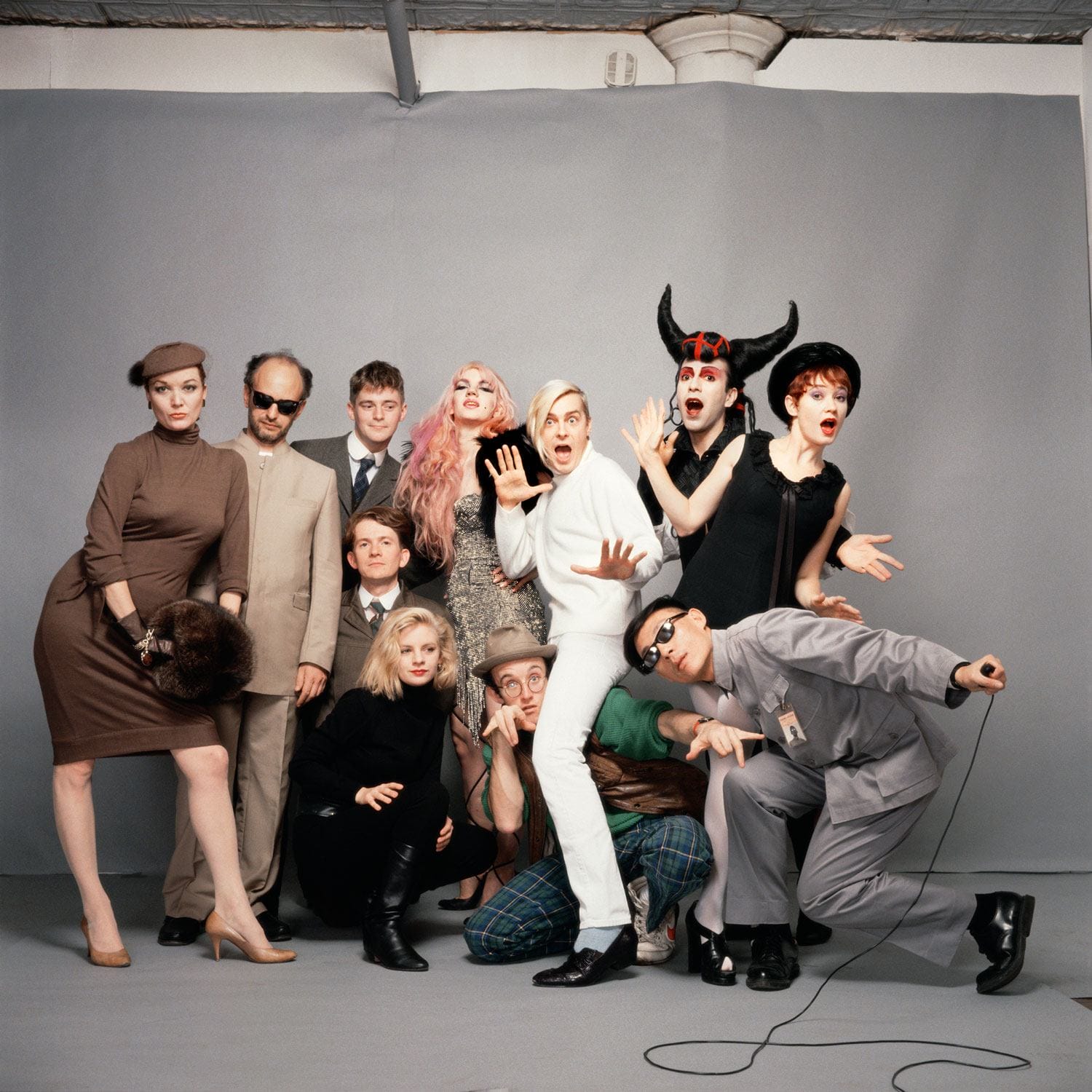 Group of people posing with various expressions and costumes against a plain backdrop in a studio setting.
