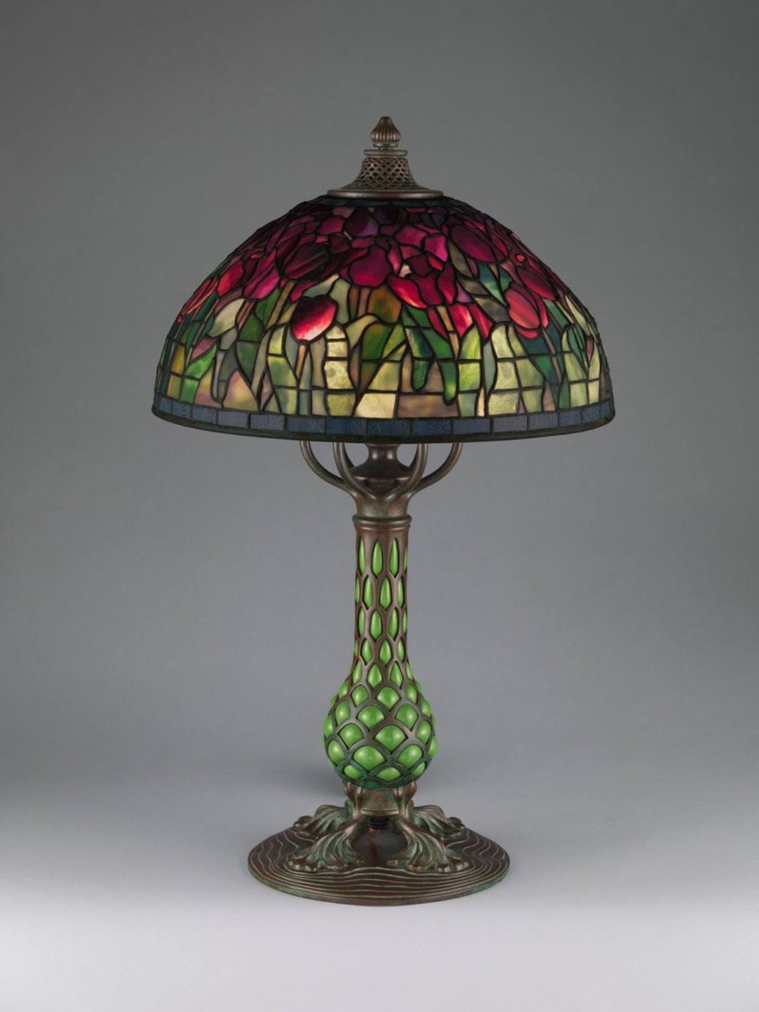 Stained glass table lamp with floral design and green base on a gray background.