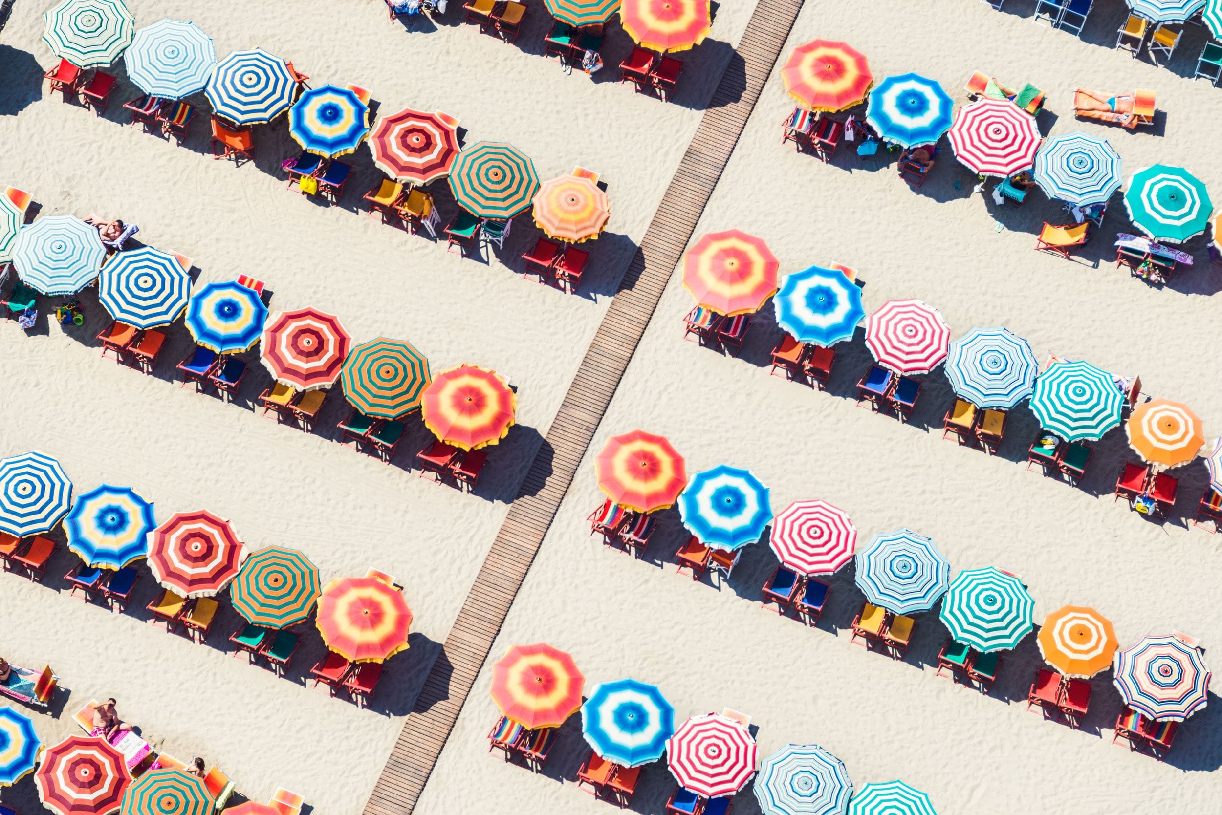 Aerial view of colorful beach umbrellas arranged in rows on sandy beach.