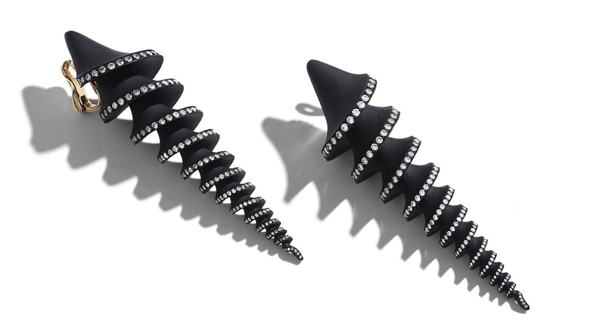 Spiral black earrings with silver studs, casting unique shadows on a white background.
