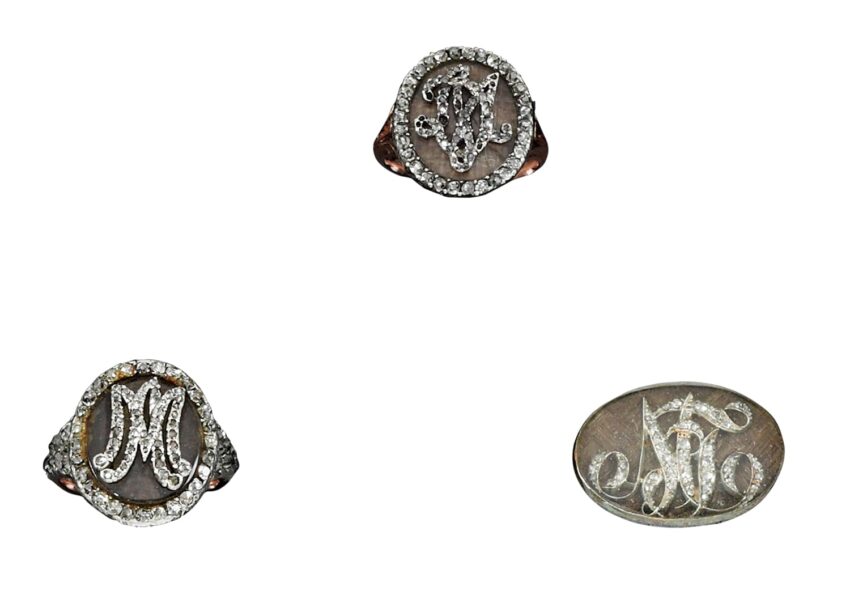 Three ornate rings with intricate monogram designs, each set with sparkling stones in a unique style.