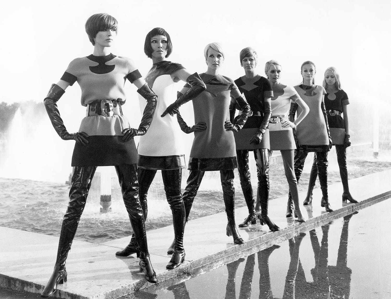 Group of women in 1960s futuristic fashion with bold designs, standing confidently near a fountain.