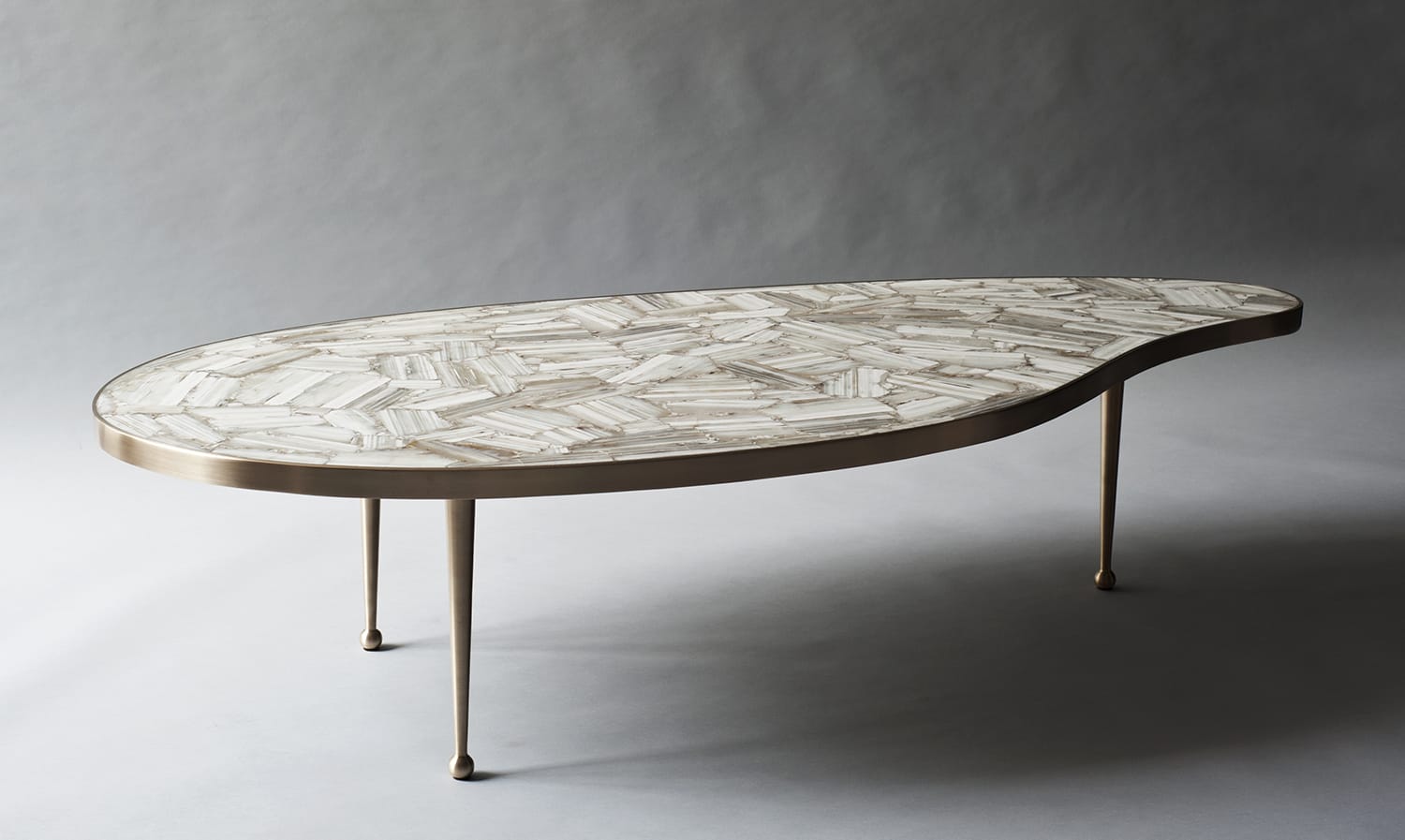 Organic-shaped coffee table with mosaic top and slender metal legs on a gray background.