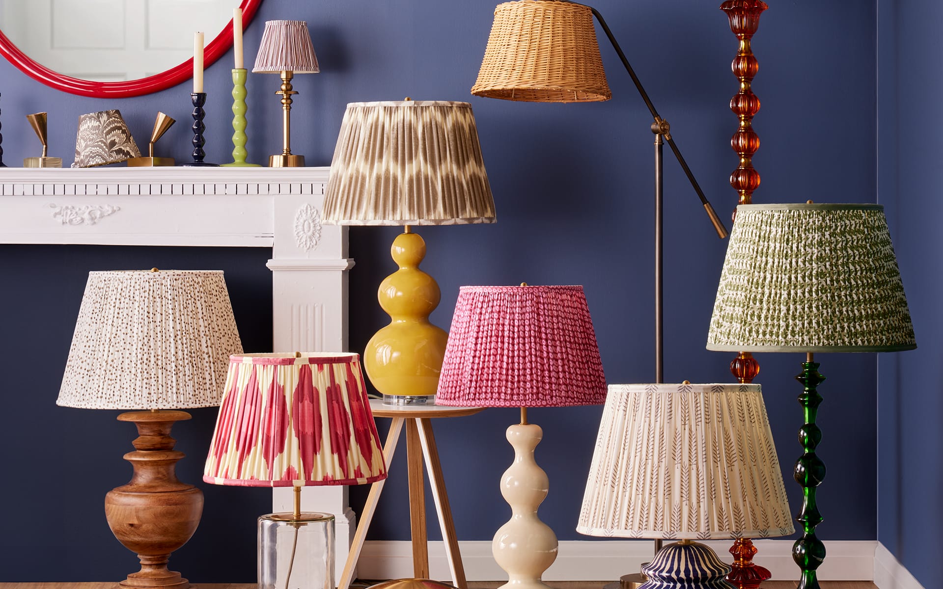 A variety of stylish lamps with colorful shades displayed in a room with blue walls and a white fireplace mantel.