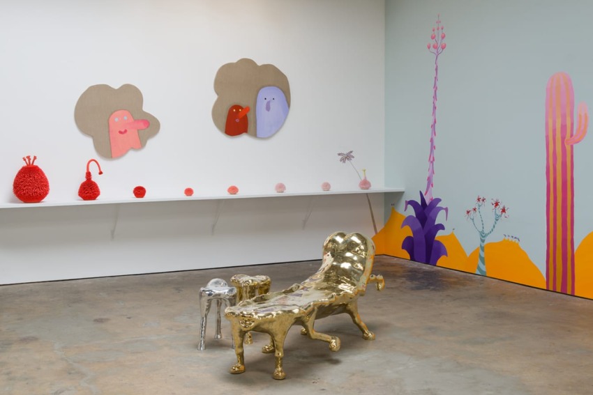 Art gallery interior with quirky gold furniture, colorful wall paintings, and whimsical artwork on display shelves.