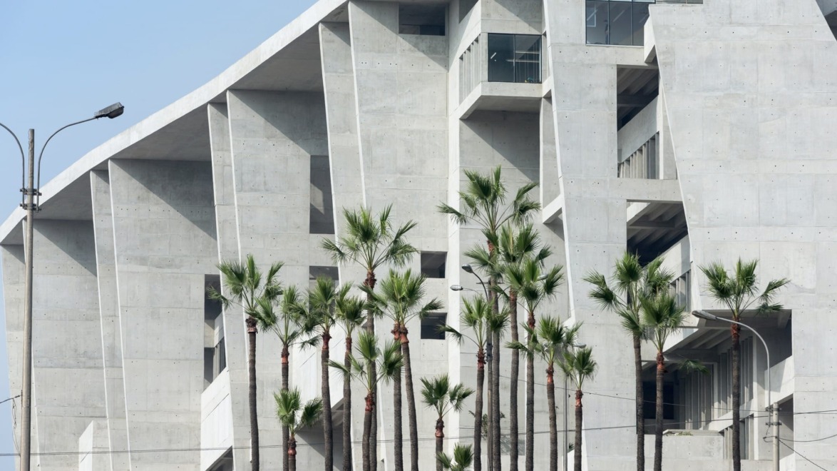 Modern concrete building with angular design features, framed by tall palm trees and a clear blue sky.