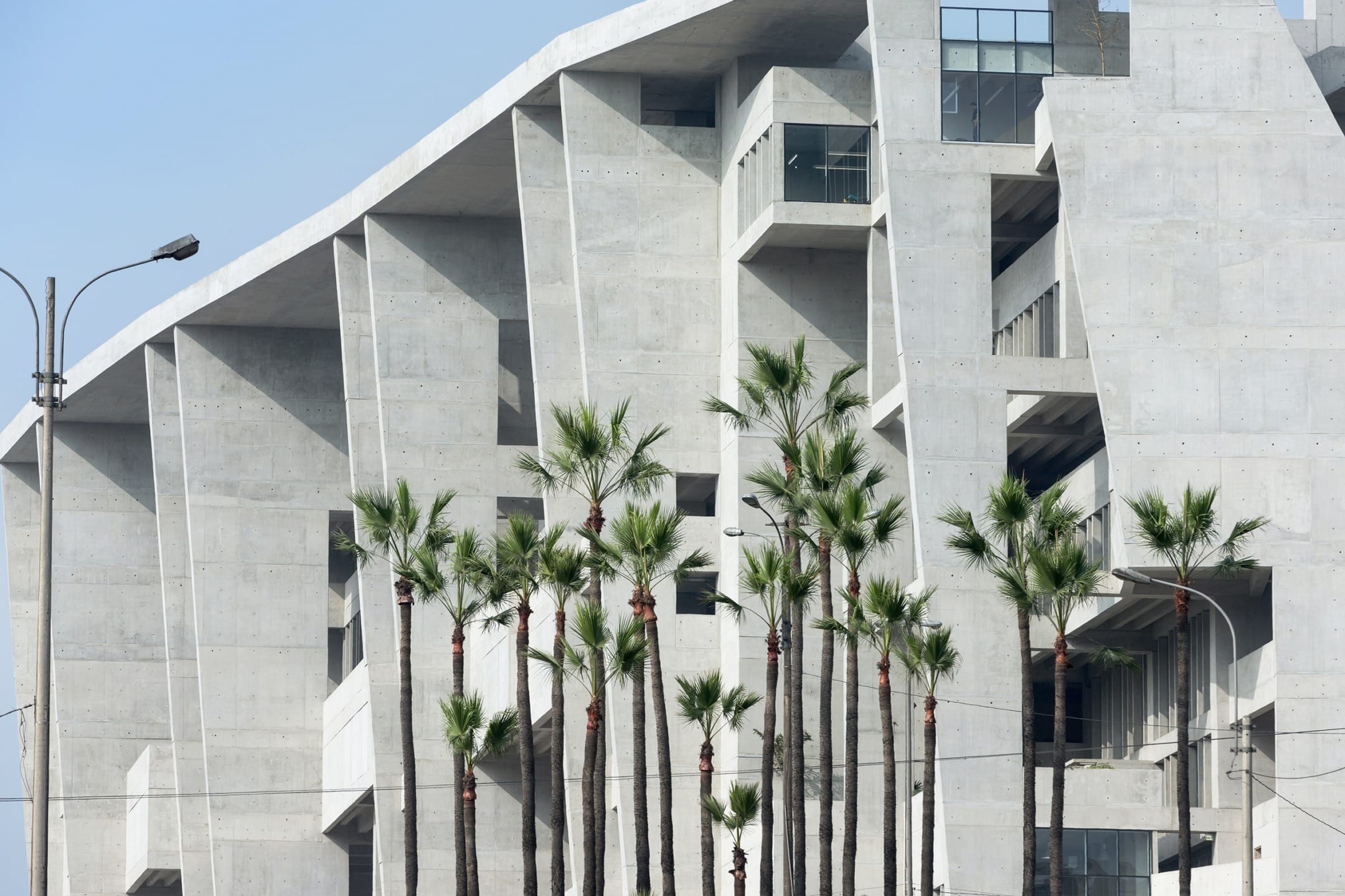 Modern concrete building with angular design features, framed by tall palm trees and a clear blue sky.