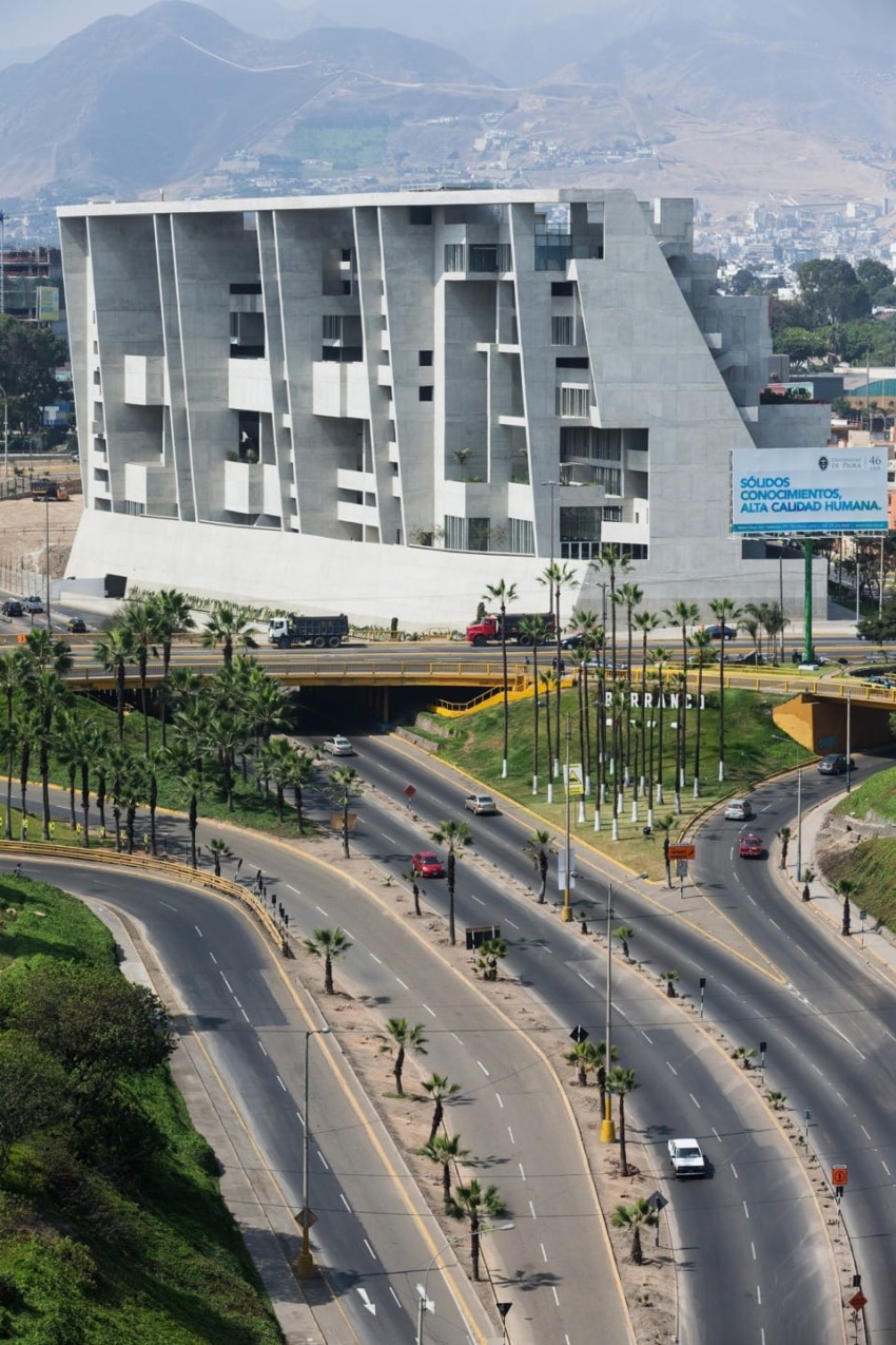 Modern geometric building beside a highway with palm trees and mountains in the background on a sunny day