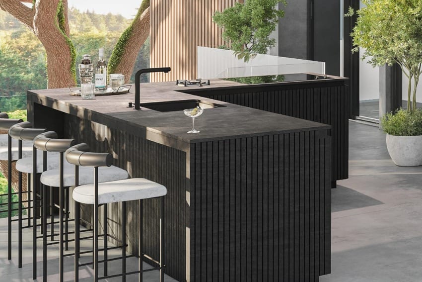 Modern outdoor kitchen with black island and bar stools, set amidst greenery and trees, with a sleek design and minimalist aesthetic.