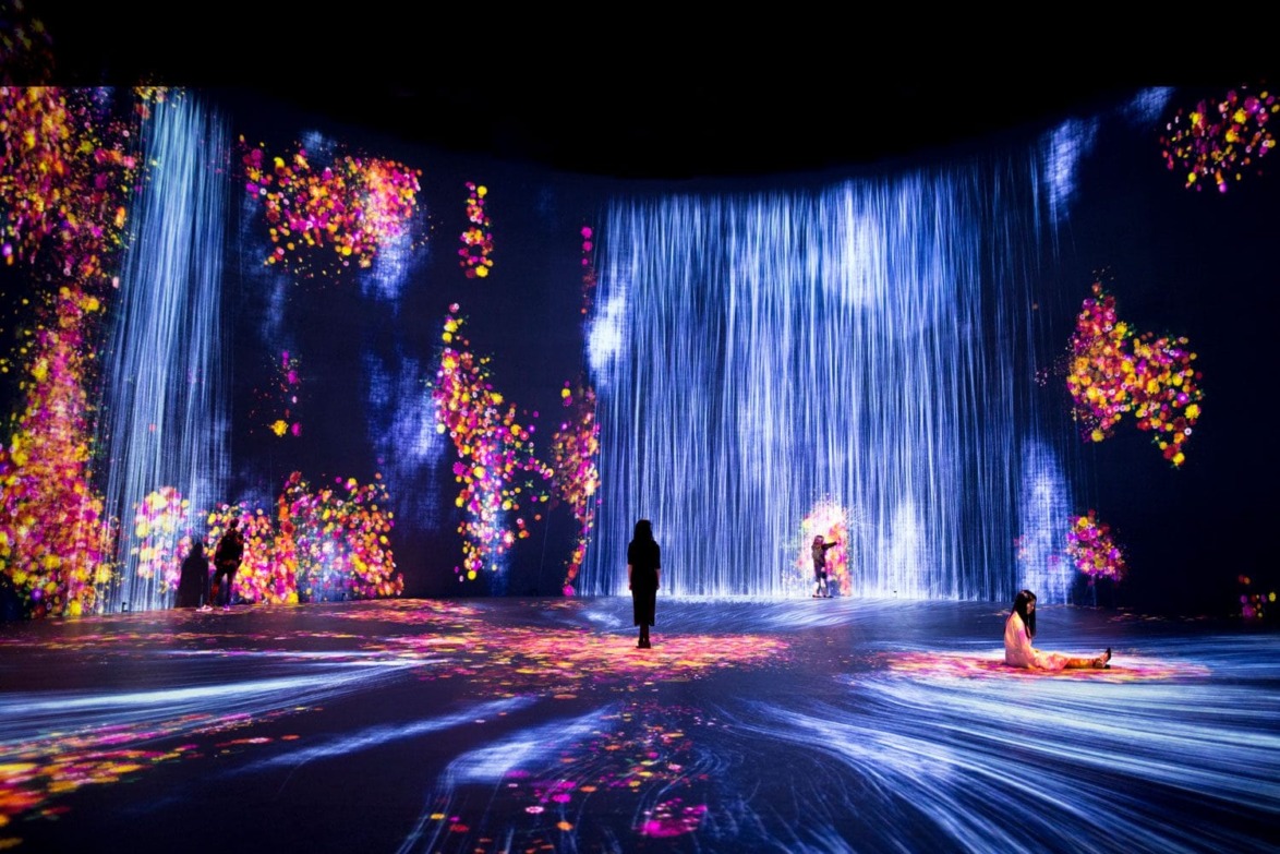 Immersive digital art installation featuring vibrant waterfalls and colorful lights with people exploring the space.