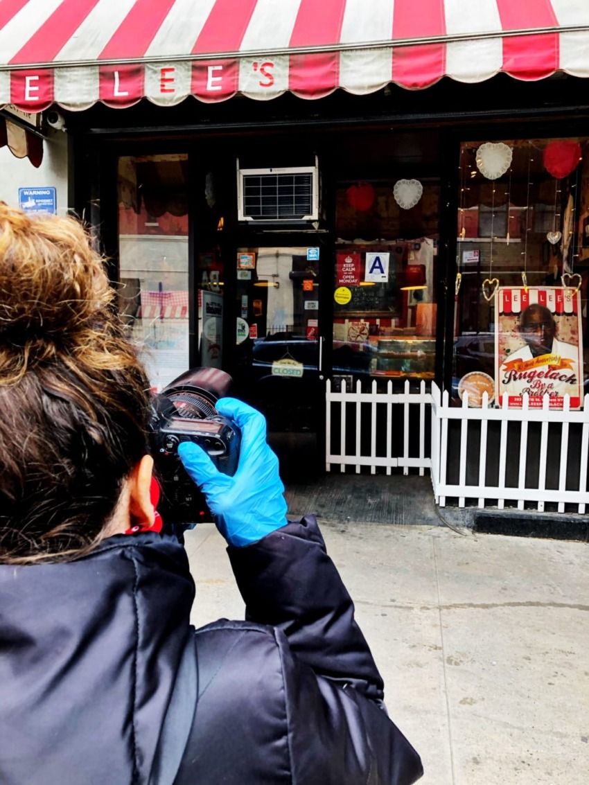 Person in blue gloves photographing a storefront with red and white awning, heart decorations, and various posters