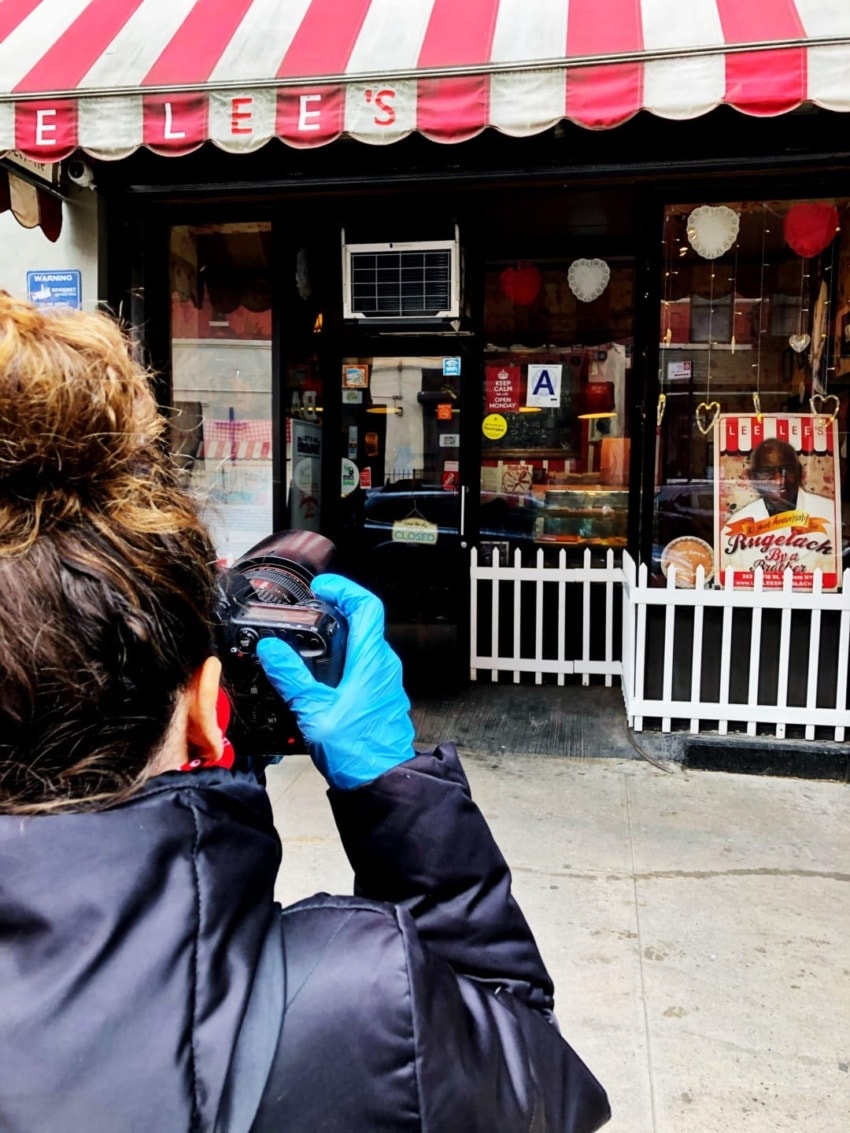 Person in blue gloves photographing a storefront with red and white awning, heart decorations, and various posters