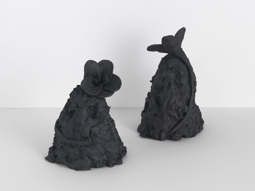 Black clay sculptures with abstract floral shapes on a white background.