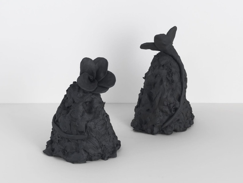 Black clay sculptures with abstract floral shapes on a white background.