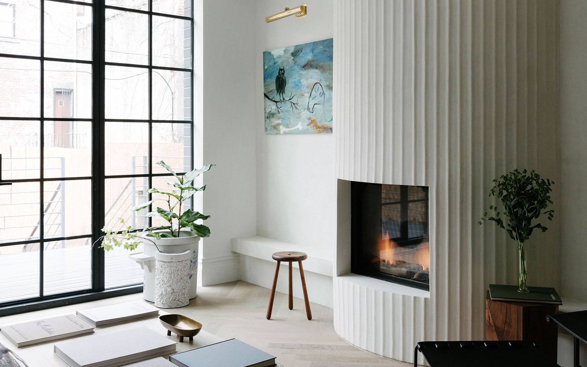 Modern living room with vertical fireplace, large windows, and elegant green plants, creating a cozy and stylish atmosphere.