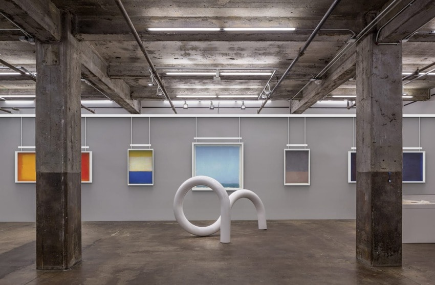 Contemporary art gallery with abstract paintings on walls and a modern white sculpture in the center of an industrial space.