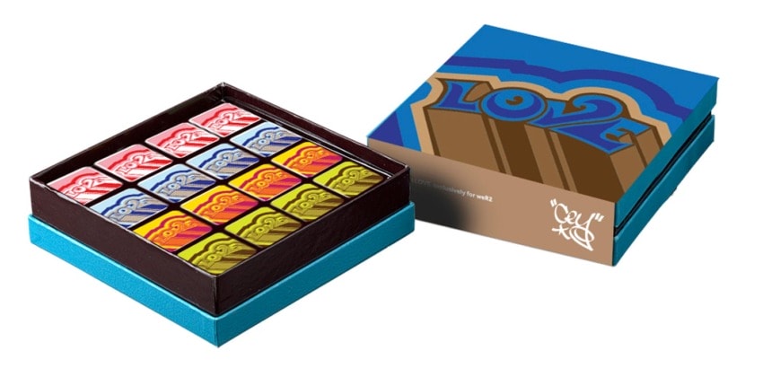 Box of colorful, artistic square chocolates with an open lid displaying the design and neatly arranged treats inside.