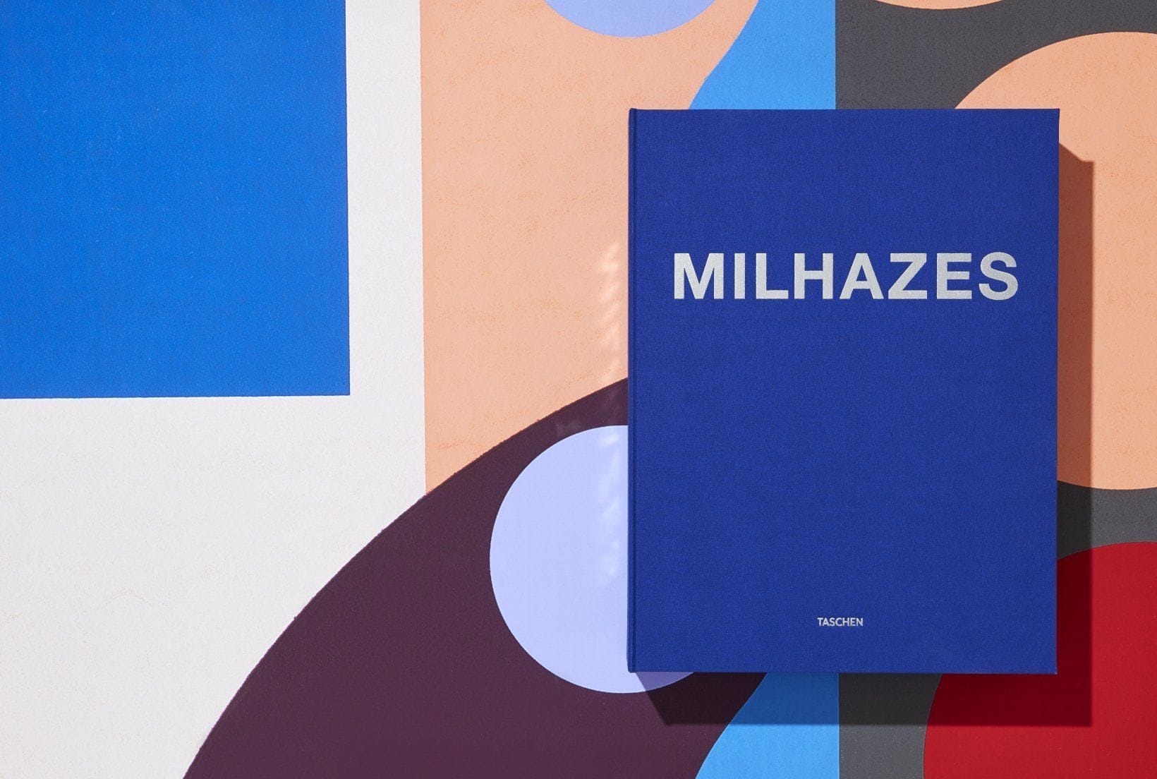 Blue book titled "MILHAZES" on colorful geometric background with orange, blue, and purple shapes.