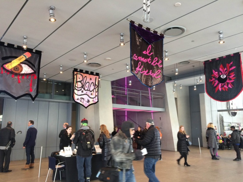 People walking in a modern lobby with colorful hanging banners featuring various designs and words.