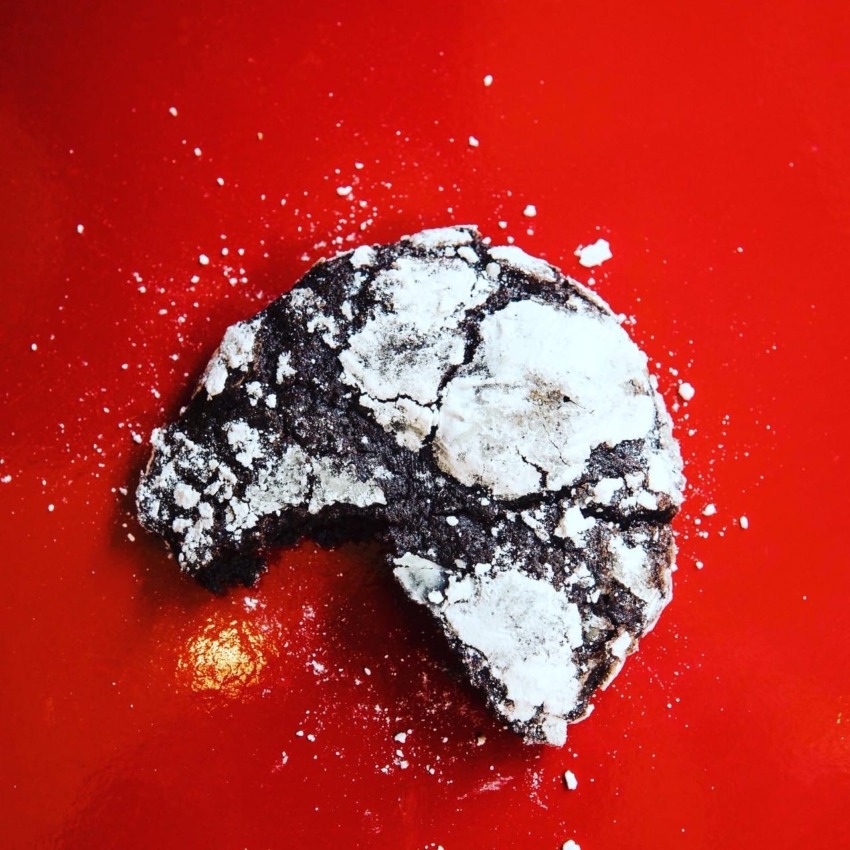 Chocolate crinkle cookie with a bite taken, dusted with powdered sugar, on a bright red background.
