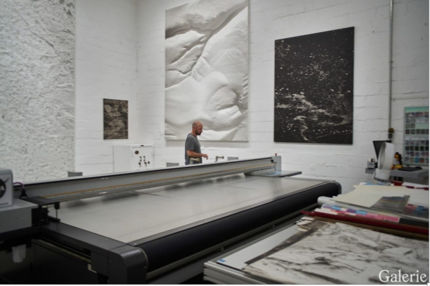 Art gallery with large scale abstract artworks on walls and a person walking near a large flatbed printer.