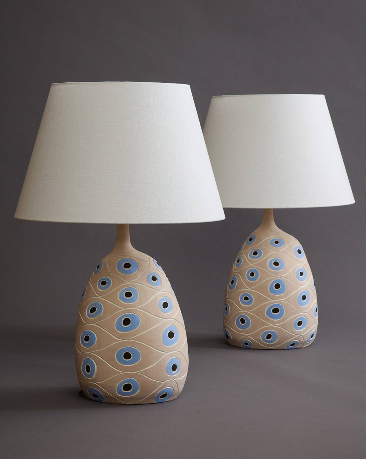 Two beige table lamps with blue circular patterns and white shades on a gray background.
