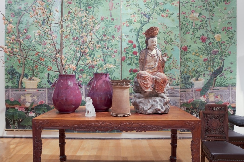 Asian art display with vases, floral screen, and seated statue on a wooden table.