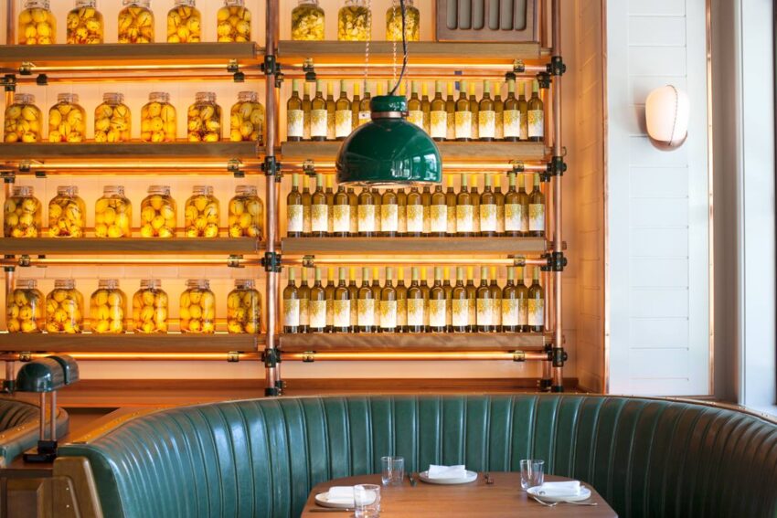Cozy restaurant booth with leather seats, wooden table set for dining, and shelves of jars with preserved fruit in the background.