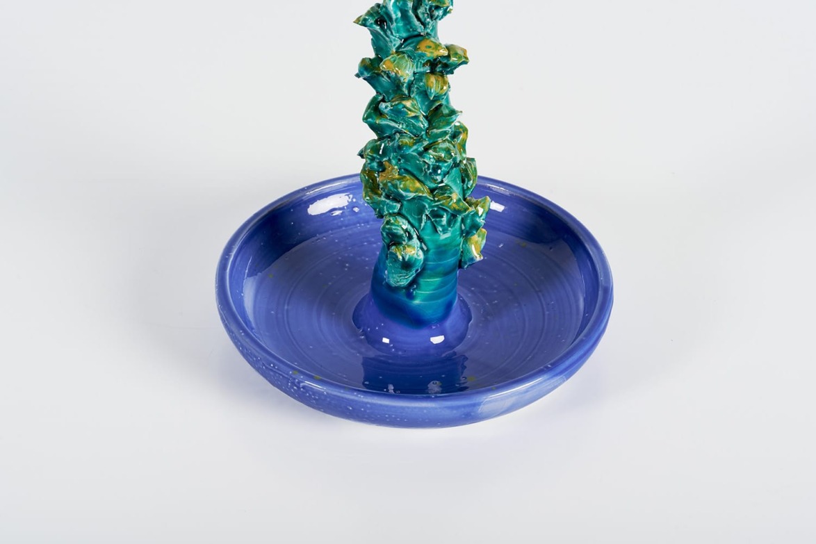 Ceramic blue bowl with a tall, textured green sculpture in the center against a plain background.