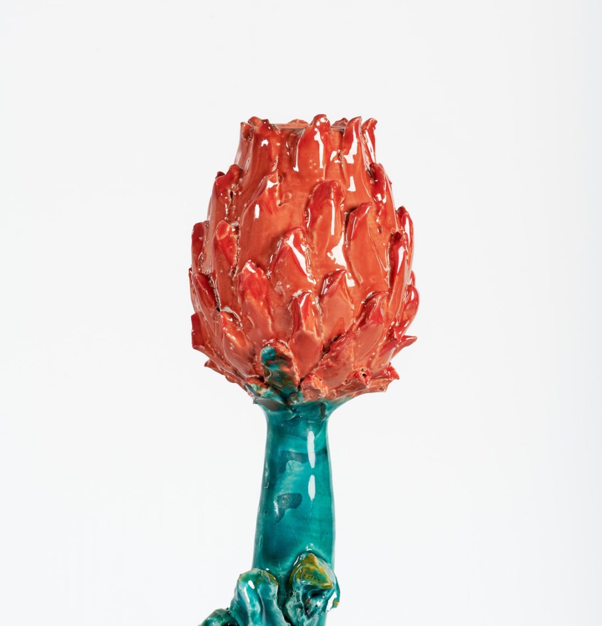 Ceramic art piece resembling a red flower with glossy finish on a teal stem, set against a plain white background.