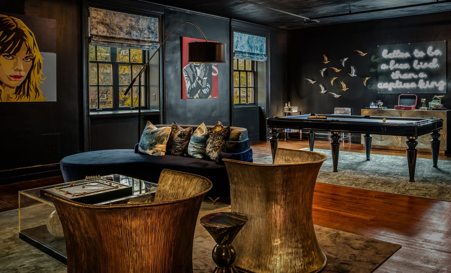 Stylish lounge with dark walls, modern furniture, pool table, and decorative art. Cozy yet sophisticated atmosphere.
