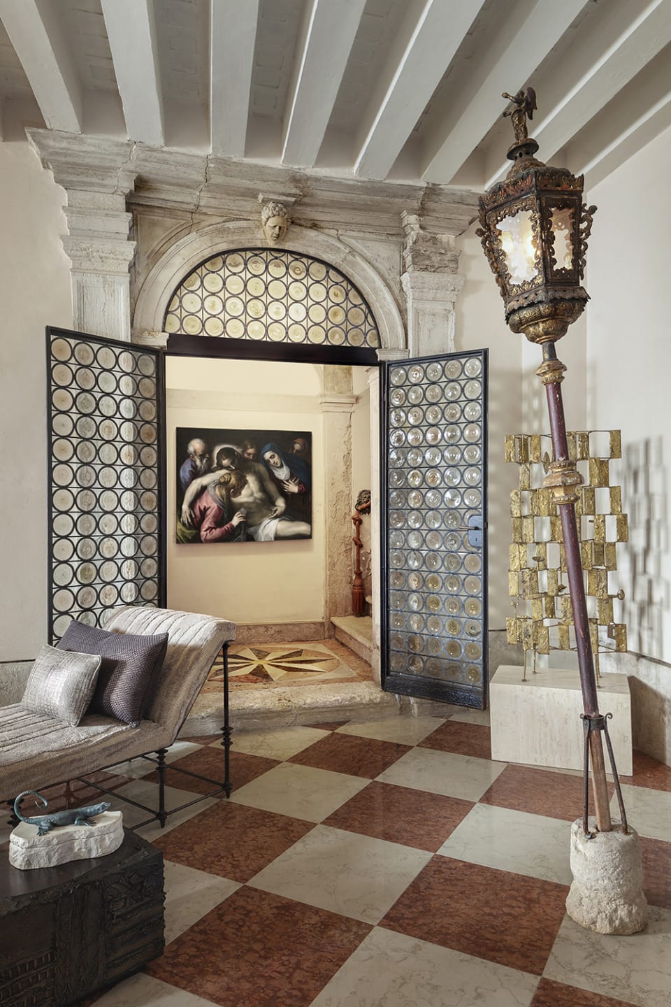 Elegant room with classical décor, featuring a checkered floor, ornate doorway, painting, and vintage lighting fixture.