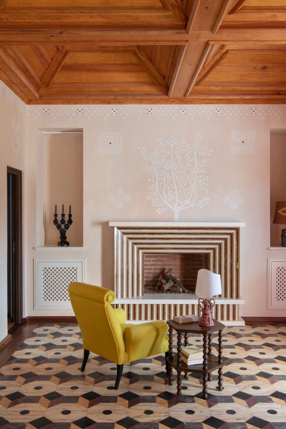 Cozy living room with a yellow armchair, geometric-patterned rug, wooden ceiling, and decorative fireplace.