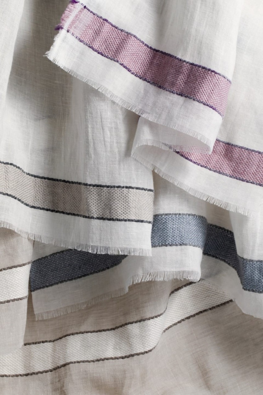 Close-up of layered white linen fabric with thin black stripes and purple accents
