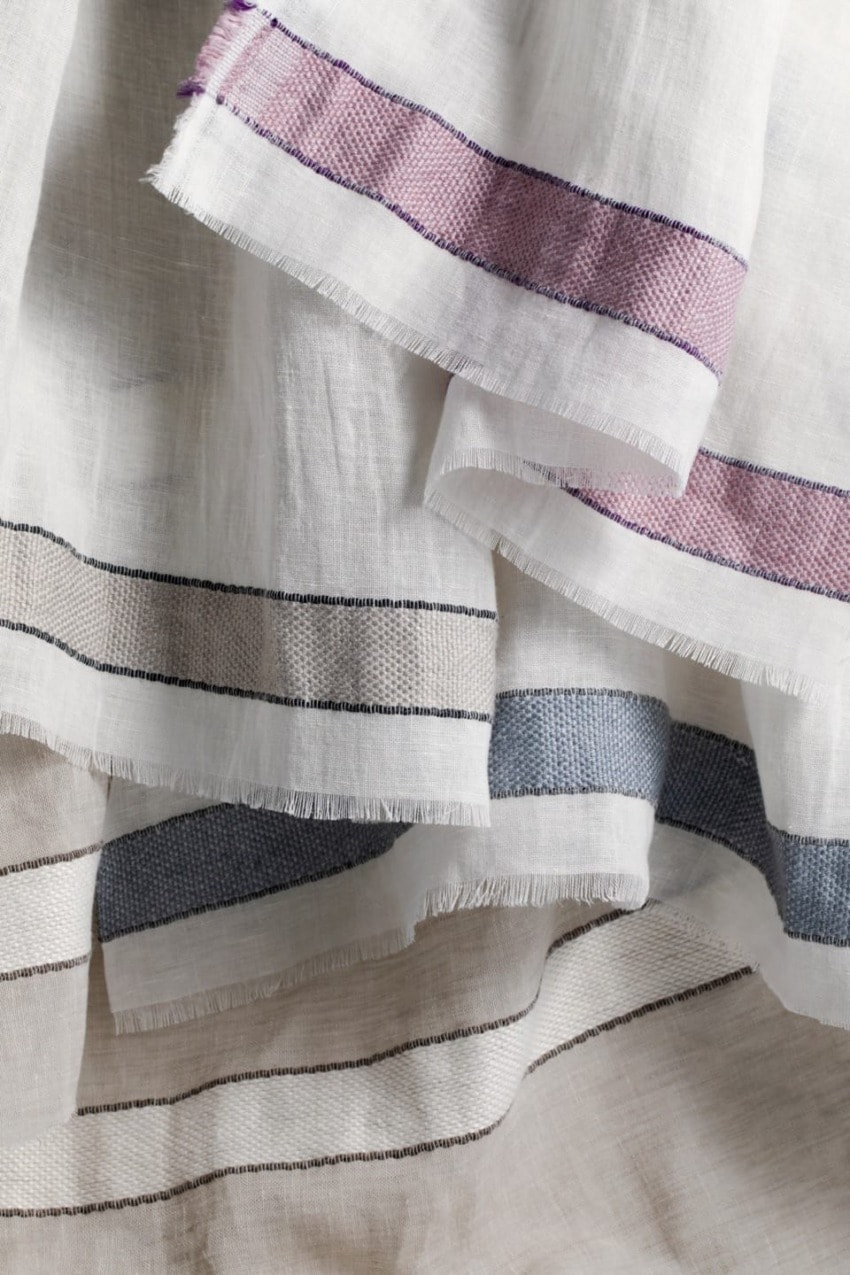 Close-up of layered white linen fabric with thin black stripes and purple accents