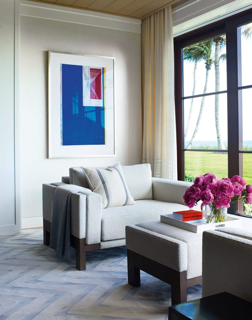 Modern living room with plush sofa, vibrant artwork, and large window view of palm trees and garden.