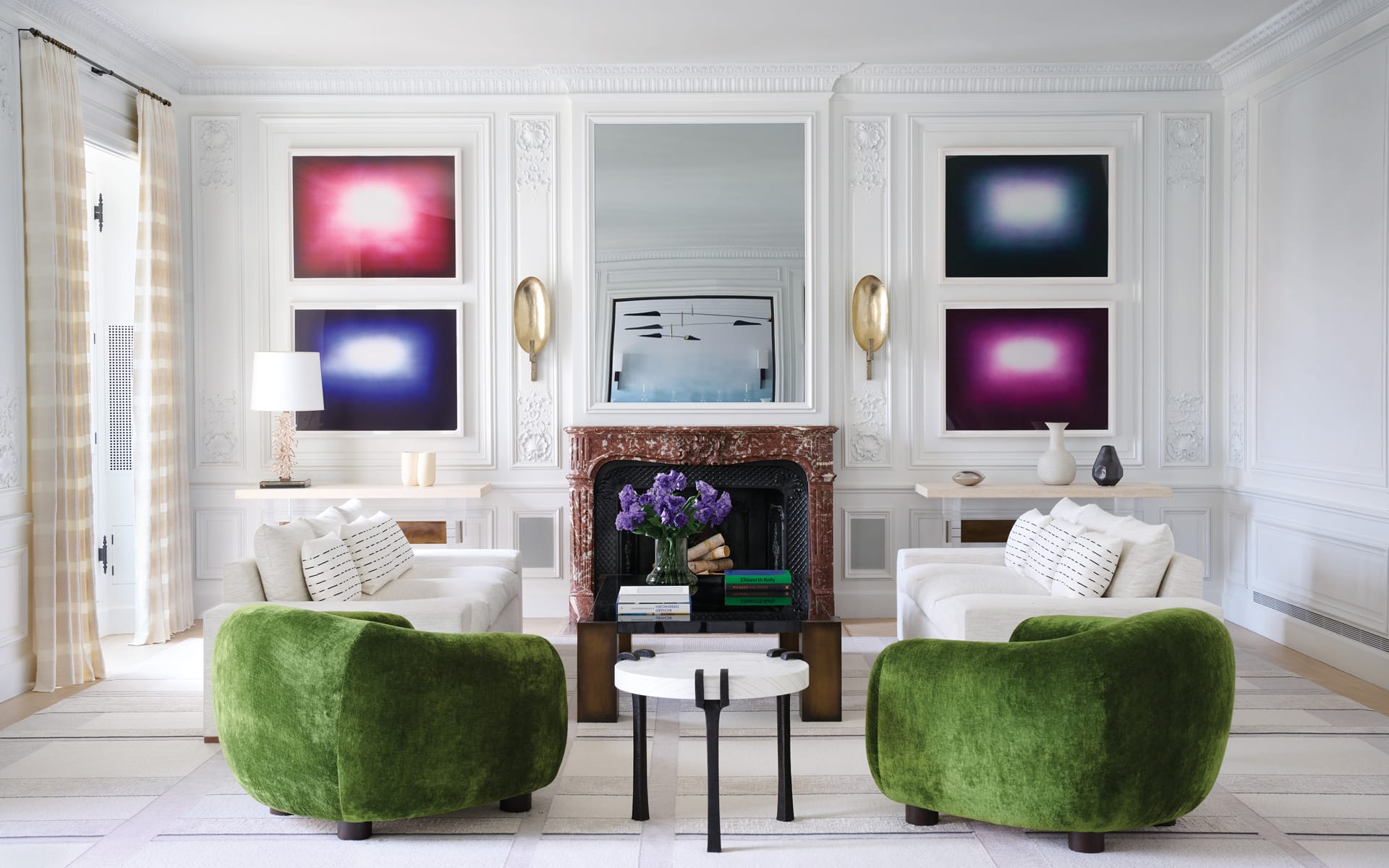 Elegant living room with green chairs, modern art on walls, and a central fireplace adorned with flowers and books.