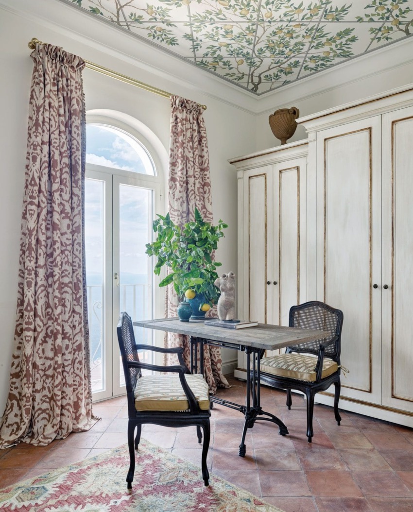 Elegant room with wrought iron table, chairs, patterned curtains, large wardrobe, potted plant, and a mural ceiling.