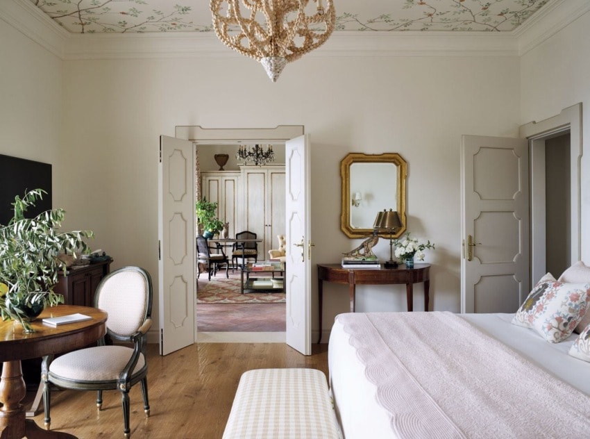 Elegant bedroom with open doors leading to a stylish living area, featuring a chandelier, decorative ceiling, and classic furniture.
